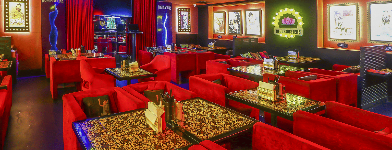 A restaurant hall with multiple red sofas, framed posters and bright neon lights at Infiniti Hotel, Indore.