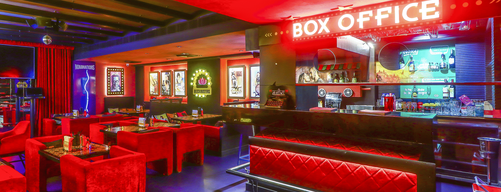 A bar counter with a glowing 'BOX OFFICE' sign and red sofas in front at Infiniti Hotel, Indore.