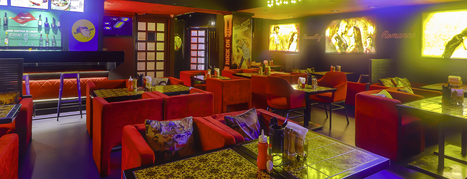 Dining tables with red sofas, decorative wall posters and a yellow neon sign at Infiniti Hotel, Indore.