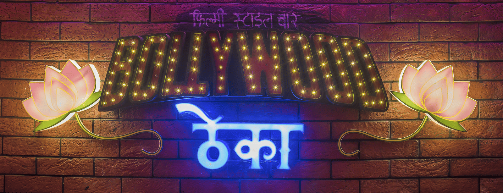 A sign reading 'Bollywood ????' with two lit flowers on a brick wall at Infiniti Hotel, Indore.
