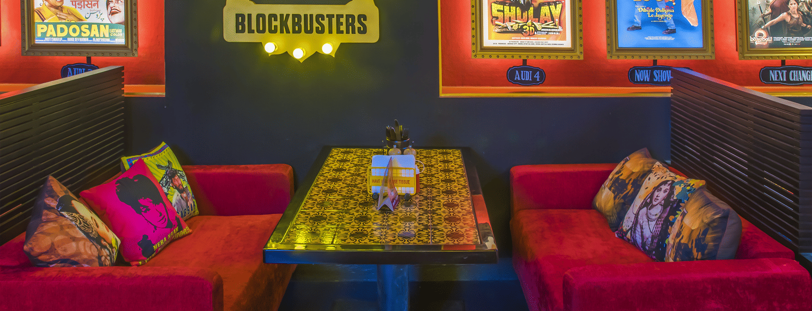 A dining table with patterned top, red sofas and framed Bollywood posters at Infiniti Hotel, Indore.