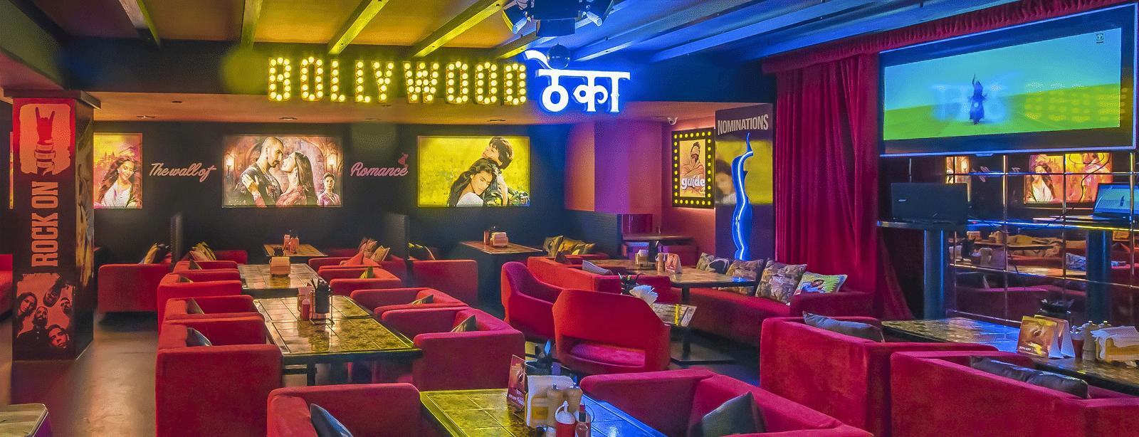 A restaurant interior with red sofas, wall posters and a glowing signboard reading 'BOLLYWOOD ????' at Infiniti Hotel, Indore.