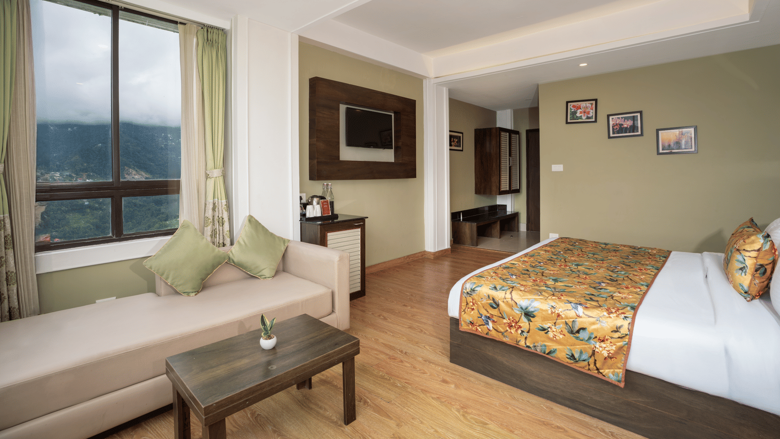 Deluxe Valley View Room at Summit North Star, Gangtok featuring a bed, a sofa with centre table, a flat TV screen, and a cabinet table.