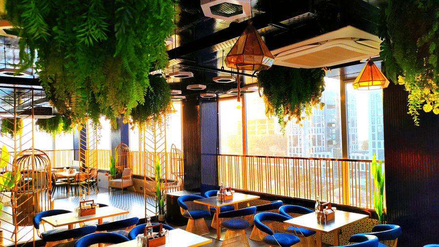 A wide-angle shot of Kensho rooftop pub at Leroy Grand, Yeshwanthpur, with sun rays filtering through the window besides the corner tables.