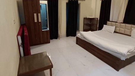 A spacious bedroom with cream-coloured walls, a large bed with white sheets, dark wood furniture including a dresser and mirror, and a black door mat on the floor | Nandan Resort