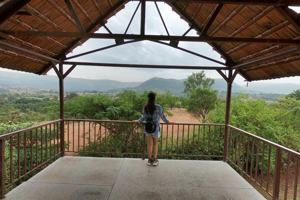 A guest enjoys the expansive view from a covered platform at Forest Escapes Koyna, overlooking the hills.