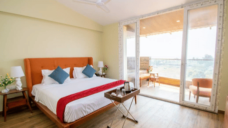 A room with a bed, a red runner, orange headboard, and a balcony with outdoor seating at Estherea Elite, Morjim.