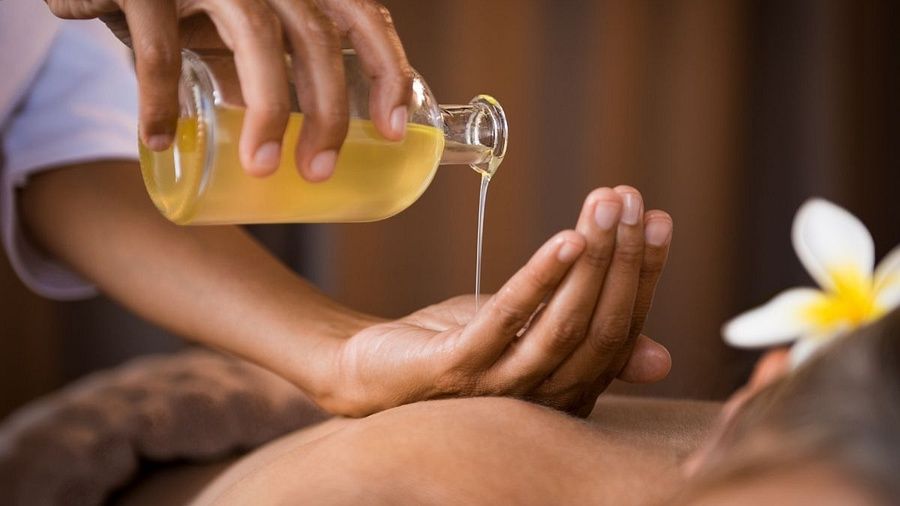 Close-up of a person pouring warm massage oil into their palm during a spa therapy session, with a flower placed beside the client.