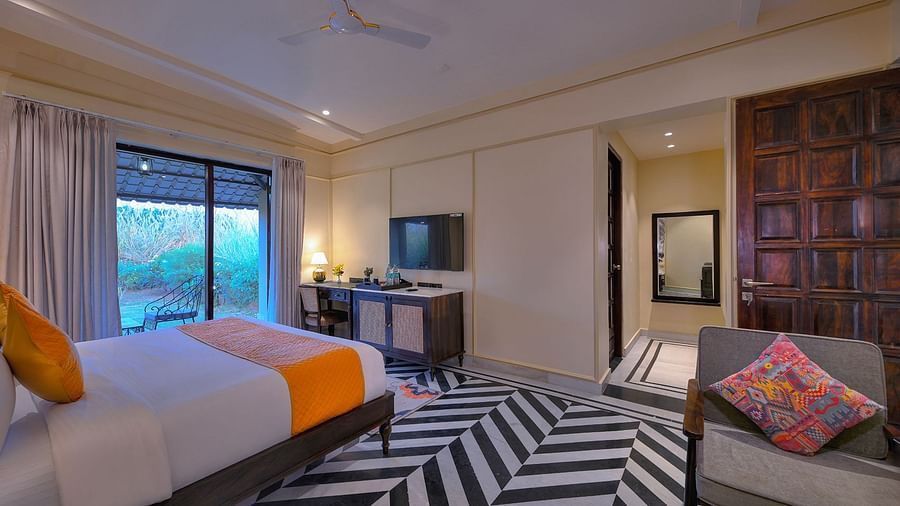 Superior Cottage with a bed featuring orange accents, black and white chevron flooring, a seating chair with a patterned pillow, a work desk, and a view to the outside - Singhvilas, Ranthambore