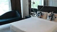A neat bed with a plush comforter. A dark chair and a side table complete the room's layout.- Golden Suites, Gurgaon