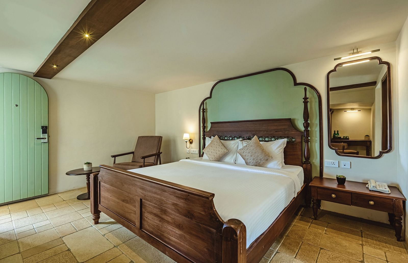 Well-lit bedroom at Mango Hill Shola, Ooty featuring a double bed with a pastel green headboard, wooden flooring, and cosy seating.
