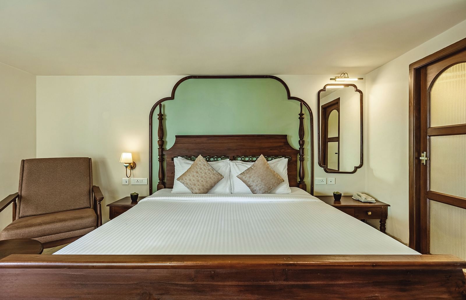 Front-facing view of the bed at Mango Hill Shola, Ooty with pastel green headboard, warm lighting, and a classic wooden design.
