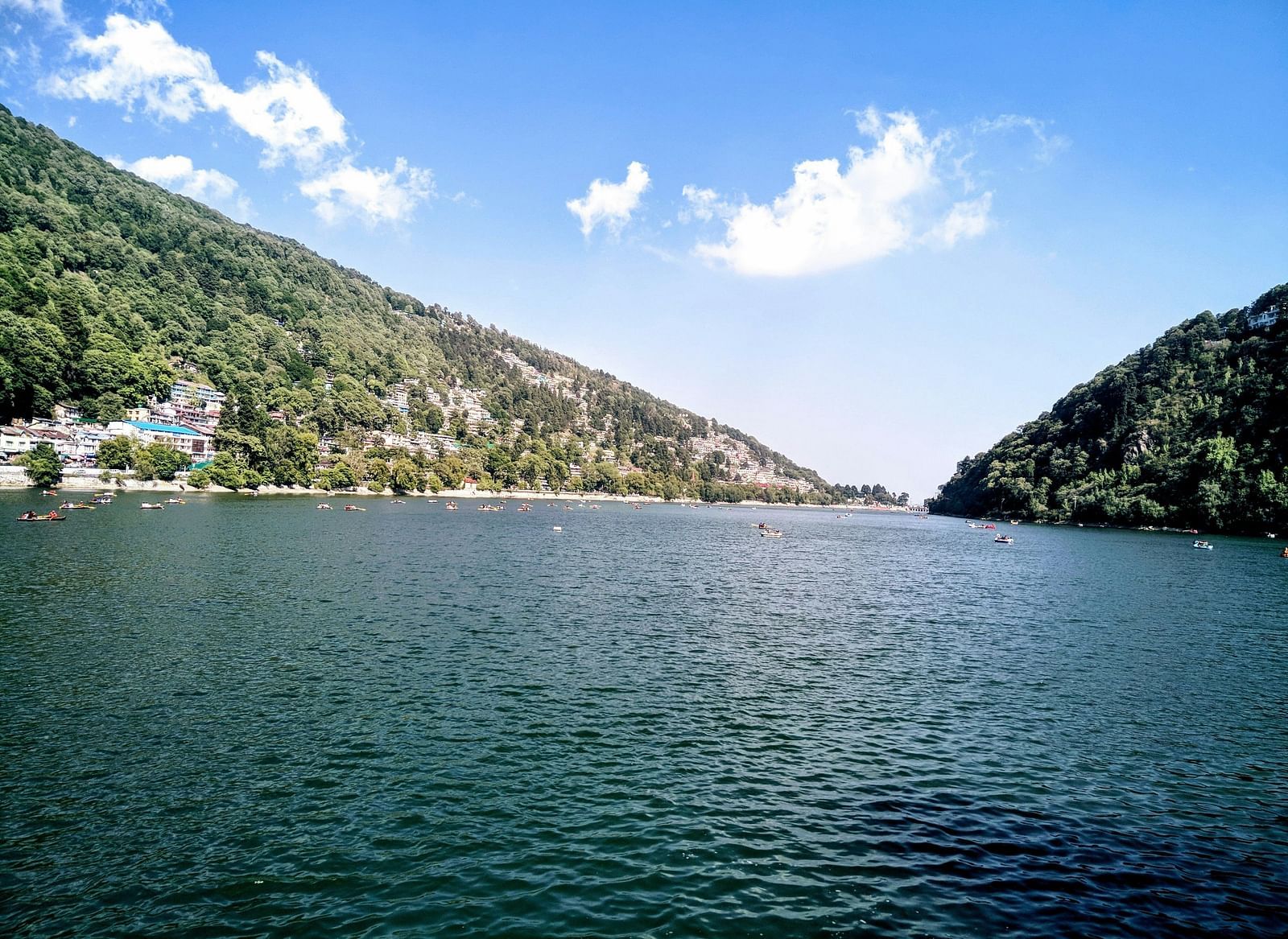 A scenic view of a lake surrounded by lush green hills under a clear blue sky.
