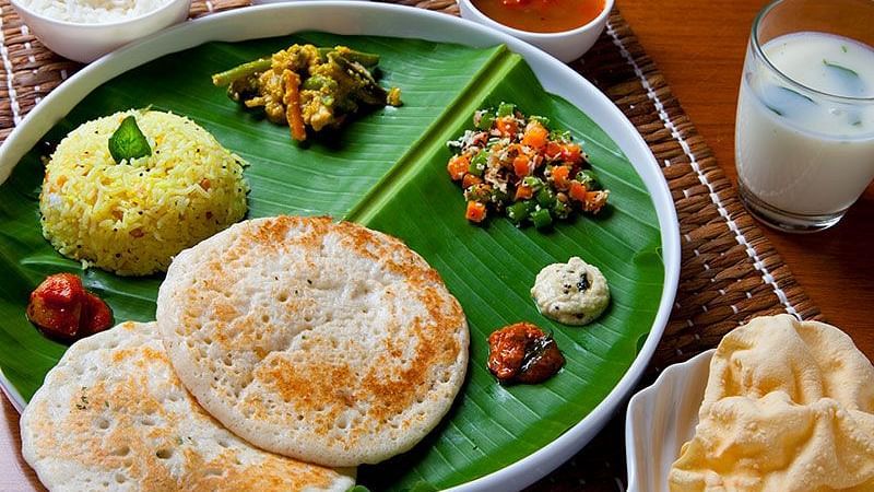 A plate of food with rice, vegetables, and flatbread on a green leaf-shaped plate - Shreyas Retreat