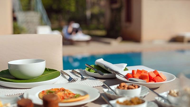 An outdoor buffet table with various dishes and a swimming pool in the background - Shreyas Retreat