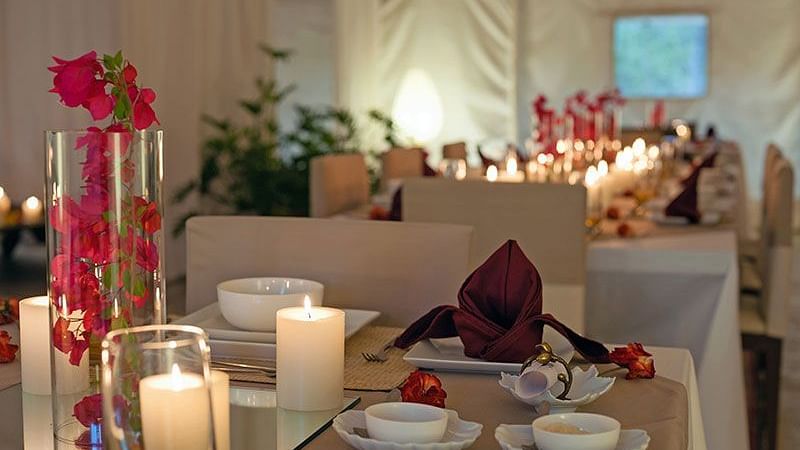 An indoor table setting with candles, flowers, and place settings - Shreyas Retreat