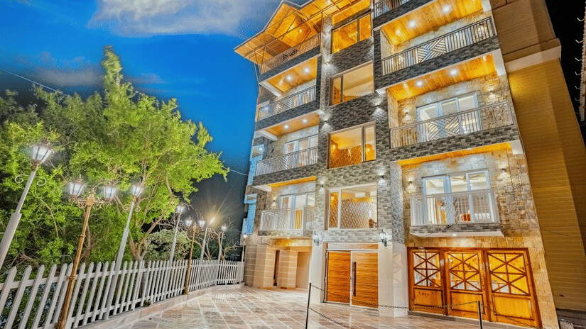 The stone-clad exterior of the hotel brilliantly lit up at night against a dark blue sky - Golden Oak By The Lake Hill, Khurpatal