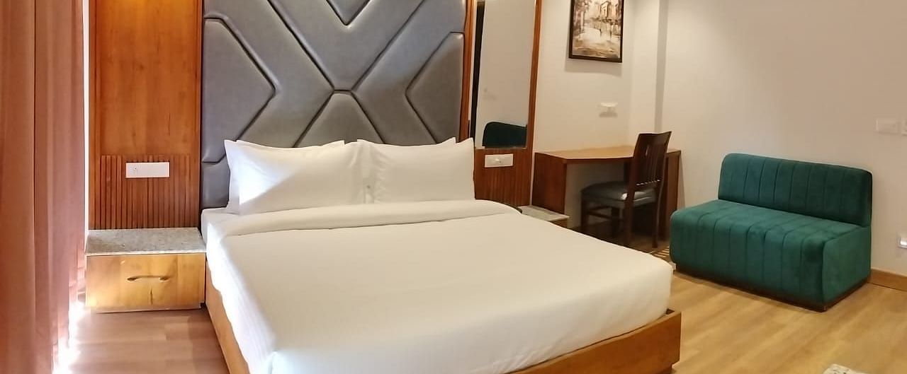 A large bed placed next to a sofa in Premium Room With Balcony at DLS Ark Holiday Inn, Banikhet.