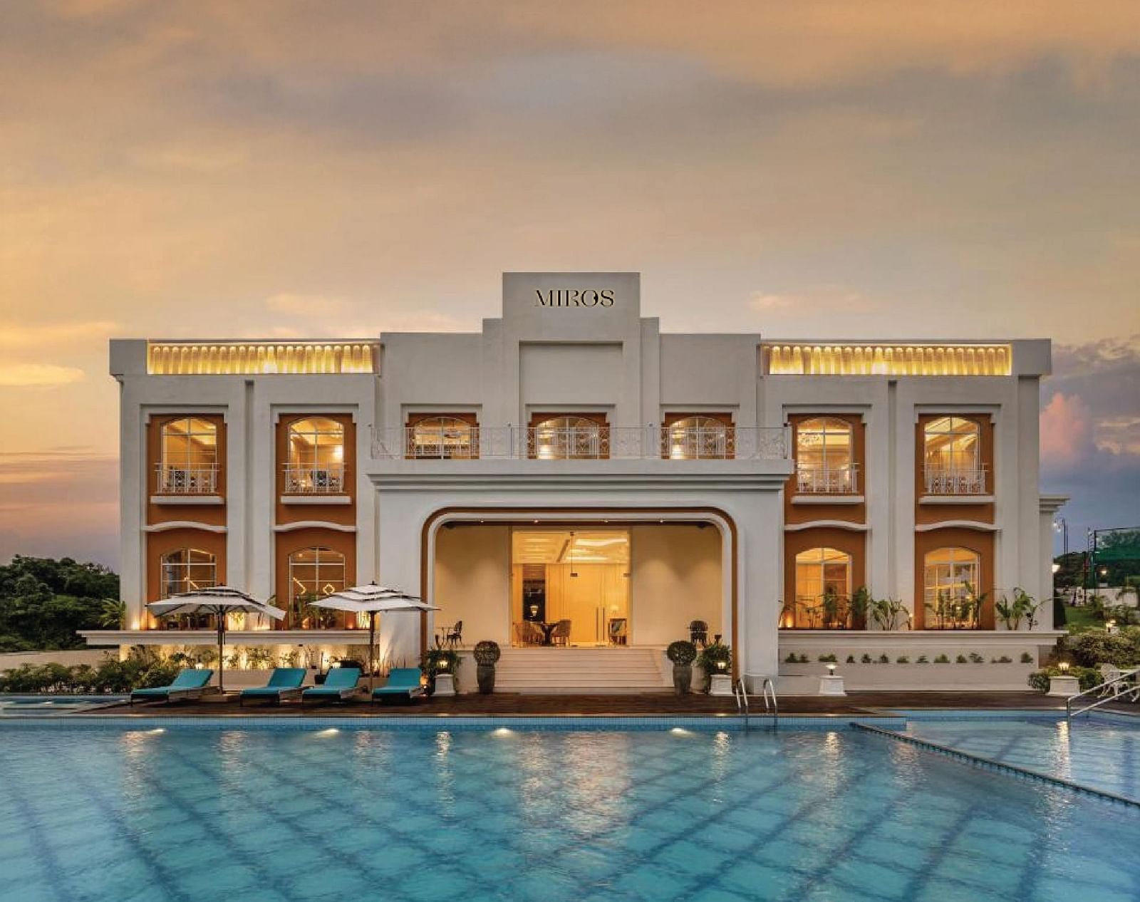 Full view facade of Miros Hotels with a calm swimming pool in the foreground along with beautiful sunset skies in the background.