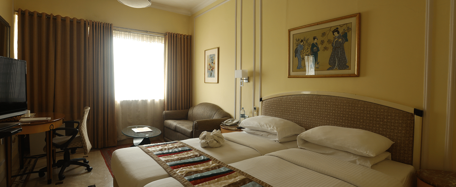 Twin beds in the Superior Room with sunlight peeking through the windows at Regency Hotel, Mumbai.