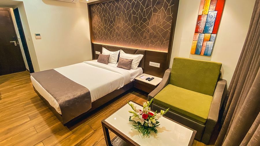 image of a bedroom with a green chair and small table on one corner and a double bed in the centre - Jardin Hotels, Indore