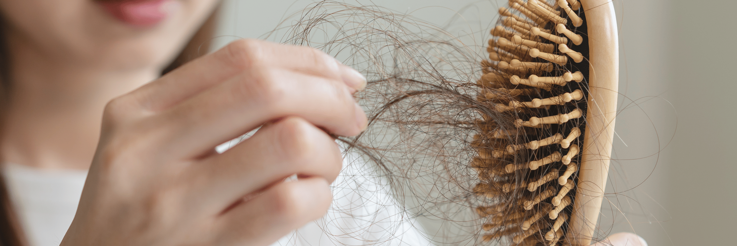 A woman holding a wooden hairbrush while pulling out loose strands of hair.