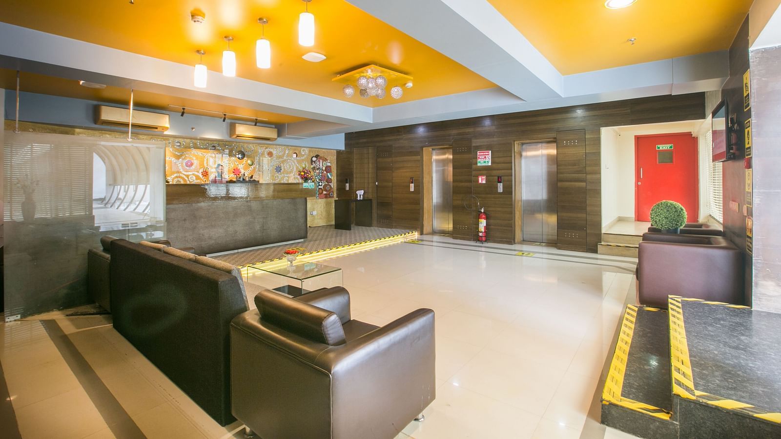 Spacious lobby with bright lighting, modern furniture, a vibrant yellow ceiling, and elevators.