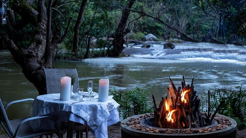 Outdoor candlelit dinner setup by a river in the evening- Amanvana Resort And Spa, Dining in Coorg