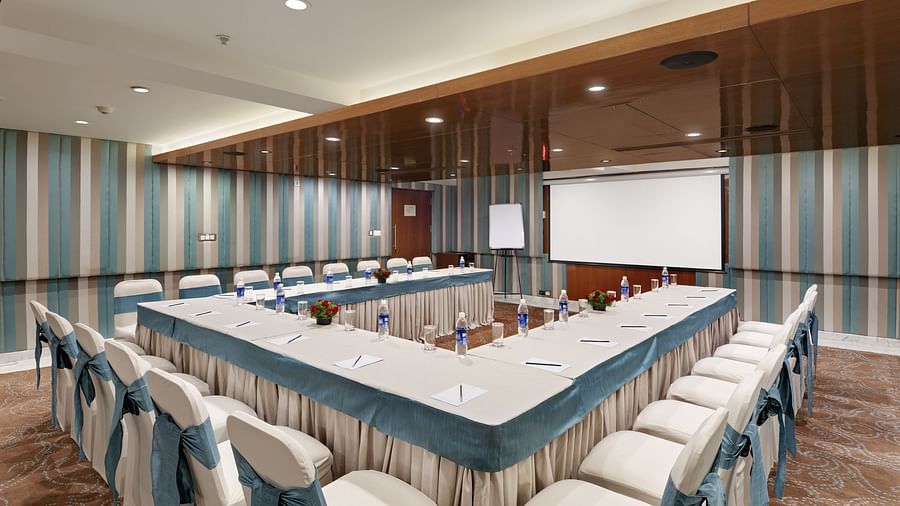Conference hall with U-shaped table arrangement and projector screen at The Elanza Hotel.