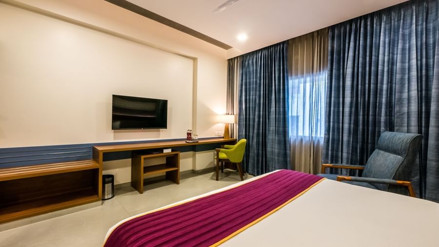 A modern hotel room featuring a comfortable bed, a desk with a television, and a cosy armchair at Shilton Dee Cee.