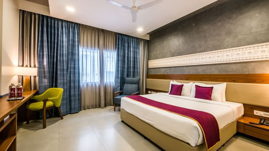 A spacious hotel bedroom with a large bed, stylish curtains, and a desk area, offering comfort at Shilton Dee Cee.