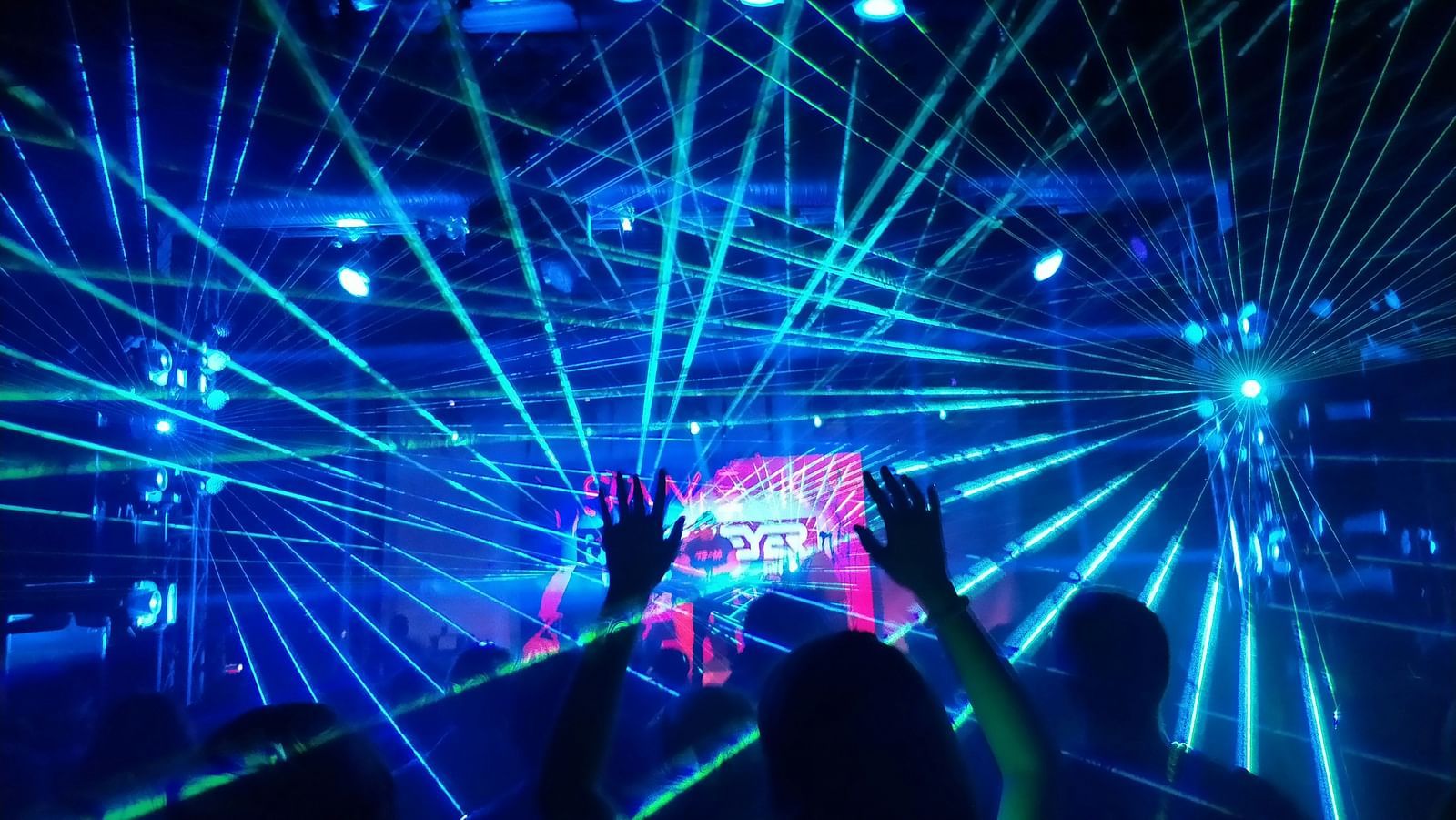 An overview of inside a nightclub with laser beams and people's silhouettes in view.
