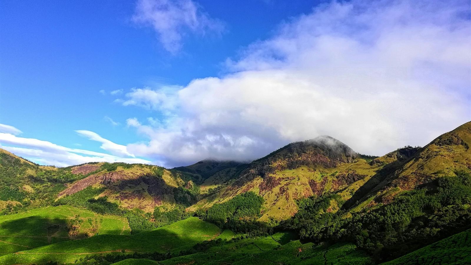 A picturesque scene of rolling green hills bathed in sunlight under a partly cloudy sky.