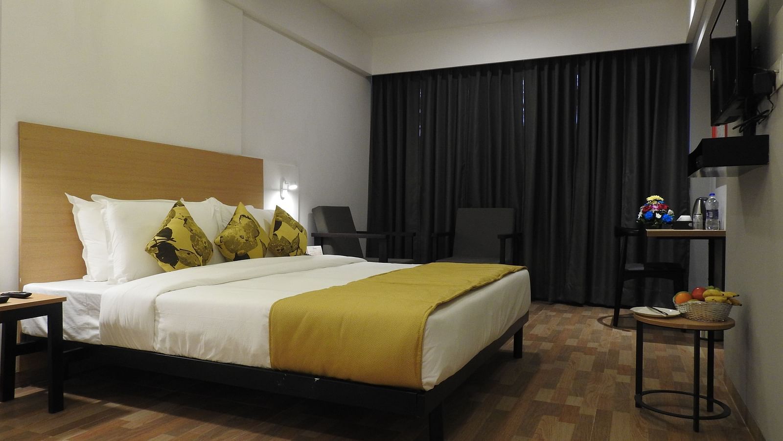 Another view of the hotel room with a double bed, gold and white bedding, a wooden headboard and a television - TGI Ameya Grand, Goa