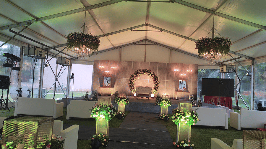 A beautifully decorated event tent with green floral arrangements, elegant lighting, and a stage set for a formal occasion or wedding ceremony - Black Thunder, Coimbatore