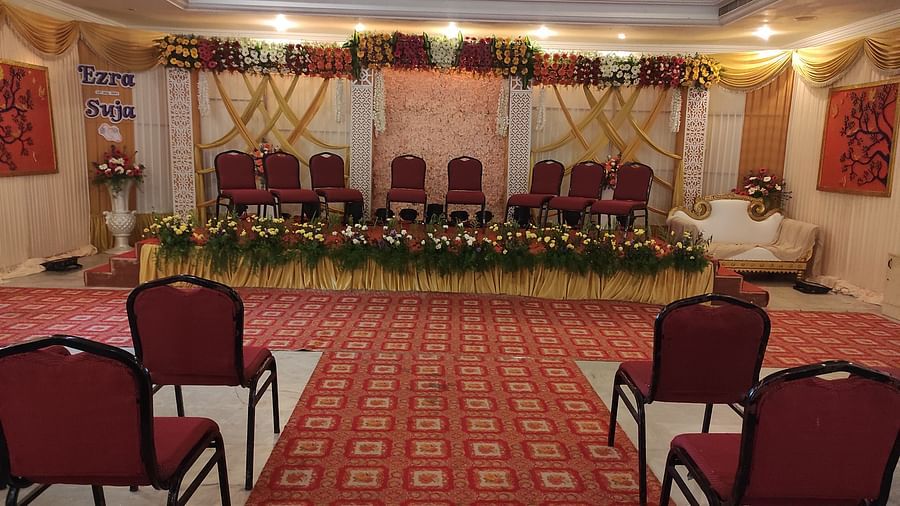 Indoor wedding or event setup with red chairs arranged in rows, facing a flower-adorned stage at the front - Black Thunder, Coimbatore