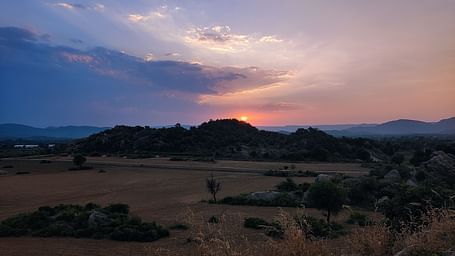 A picture featuring a range of mountains and sunset, with both dry and green land