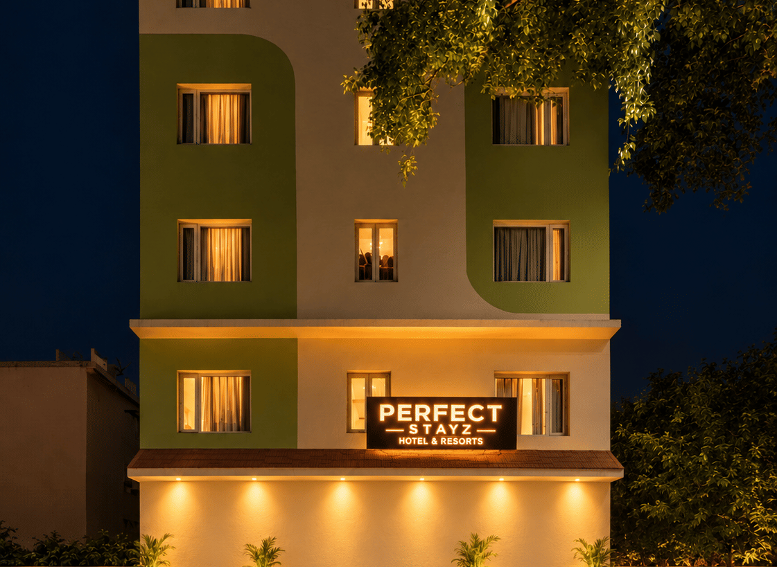 Hotel facade at night with warm window lighting green and cream walls a rooftop canopy and an illuminated sign