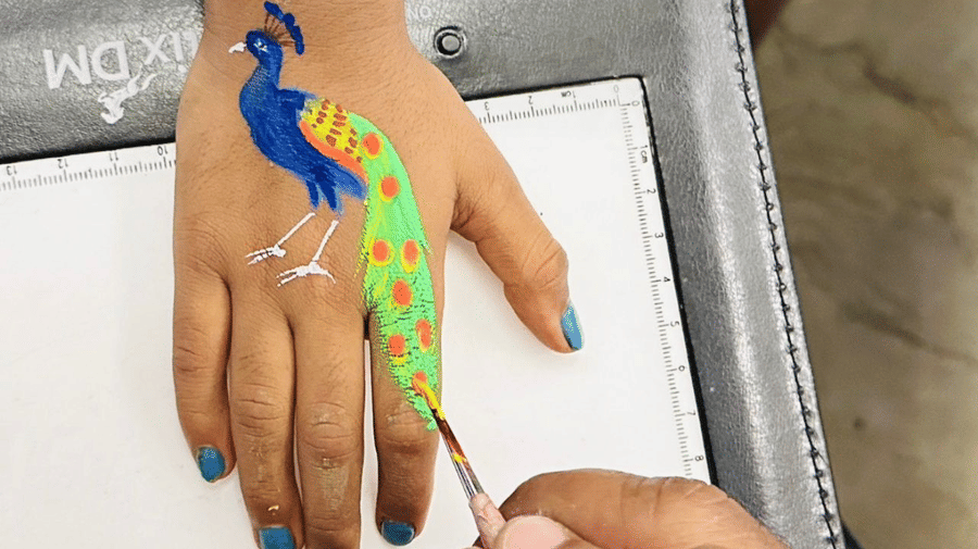 A close-up view shows a hand being painted with a colourful bird design at Amantra Shilpi Resort, Udaipur.