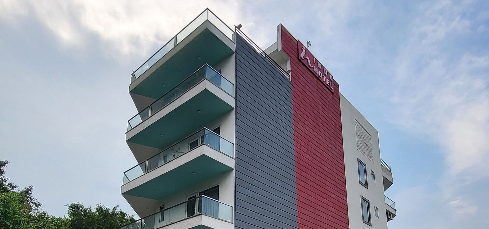 A facade of Inde Hotel Golf Course Extension featuring multiple storeys and balconies on each floor, and cars parked on the lawn