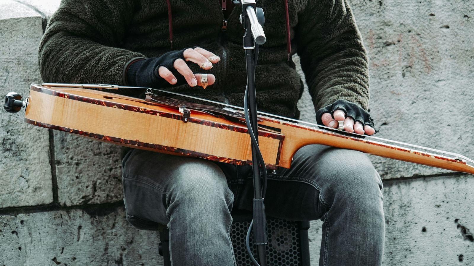 a street musician sitting on and singing through the microphone while playing the guitar