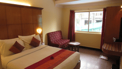 A Club Room at the best resort in Bangalore with a king sized bed, lamps, chairs, and windows with curtains | Ramanashree California Resort