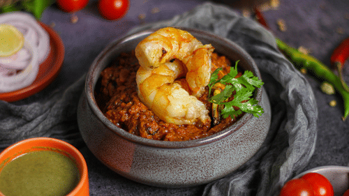 A bowl of biryani  is shown with prawns, tomatoes, and a side of green sauce.