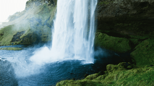 Waterfall next to mossy rocks with mist rising from the waterfall in view