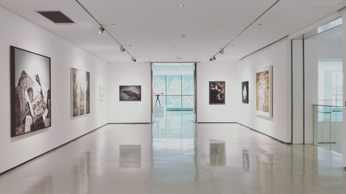 An interior of a museum with paintings hung on the walls with marbled floor reflecting a few paintings.