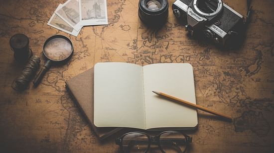 A camera, magnifying glass, notebook, pencil, glasses, etc kept on a brown, vintage-looking map