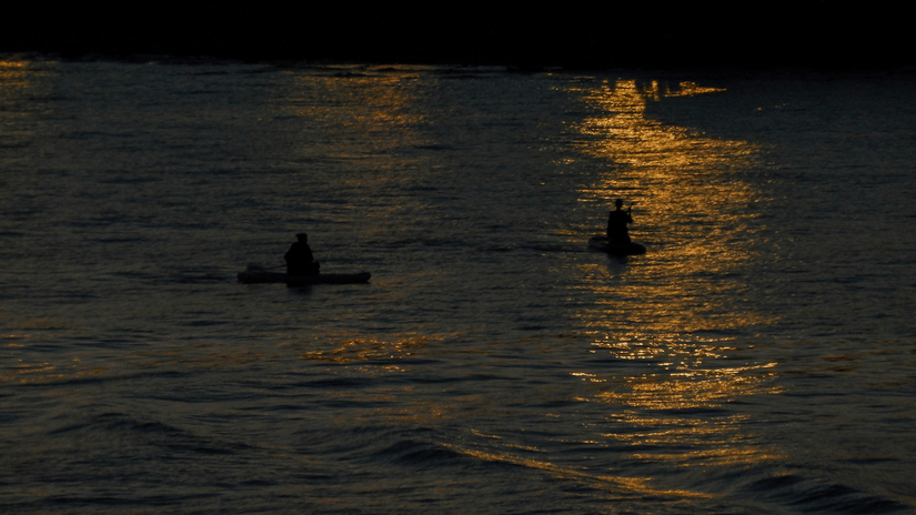 An aerial view of two kayaks travelling on a waterbody with reflection of a light on the water.