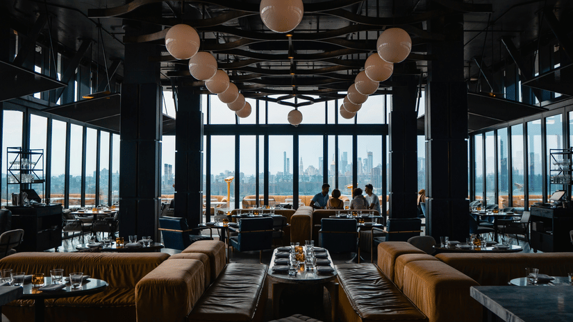 Modern rooftop lounge with floor-to-ceiling windows, stylish seating, and panoramic city skyline views