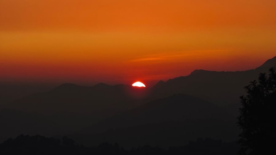 The sun sets behind a distant mountain peak, casting a warm, golden glow across the landscape, creating a sense of depth and tranquillity, possibly a view from the resort