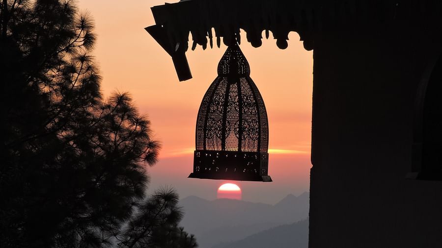 A silhouetted roofline frames the setting sun, with a decorative birdcage hanging gracefully, capturing a charming architectural detail against the warm glow of twilight, possibly a feature of the resort surroundings